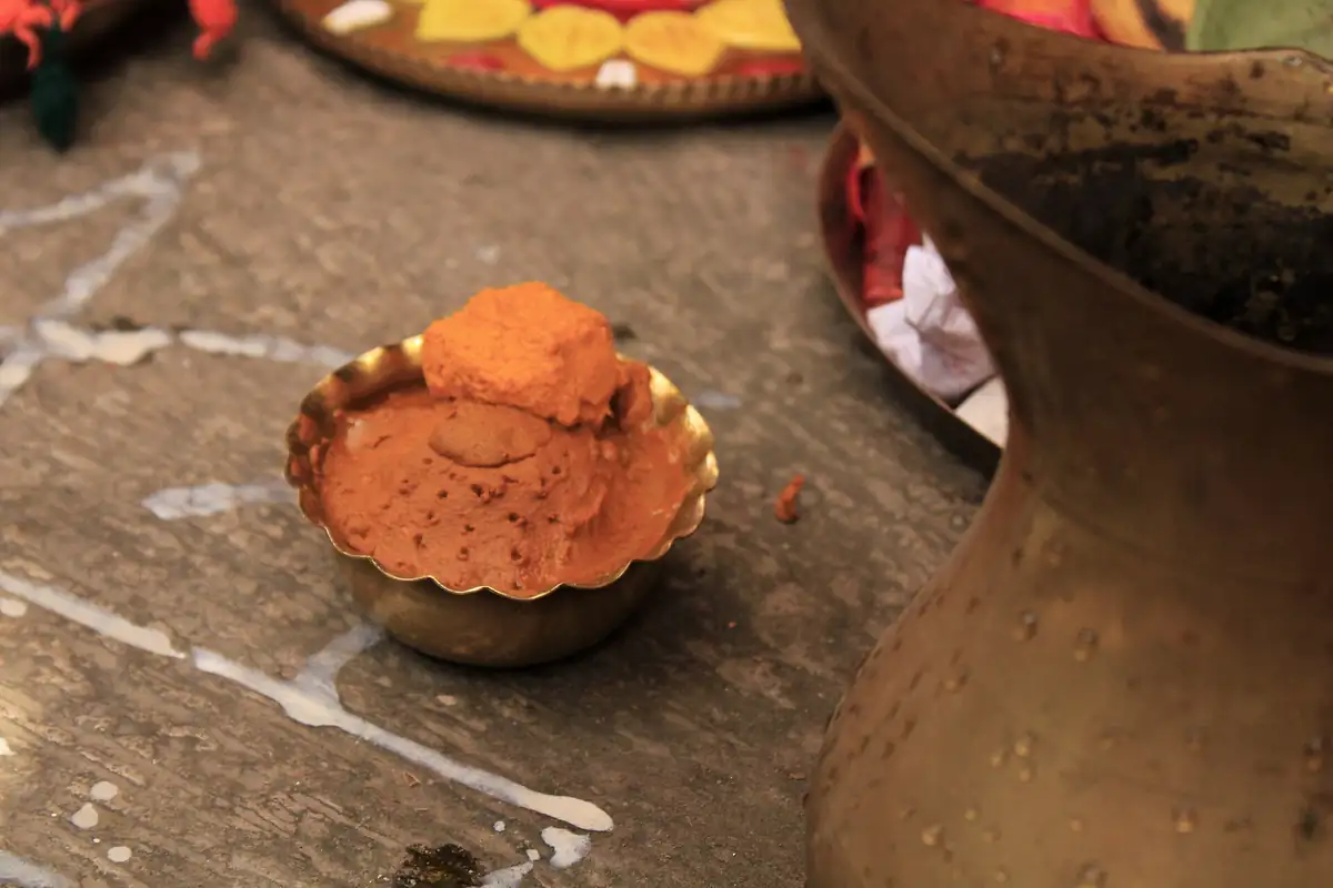 A brass bowl of fresh turmeric paste on a kolam-marked floor before the haldi