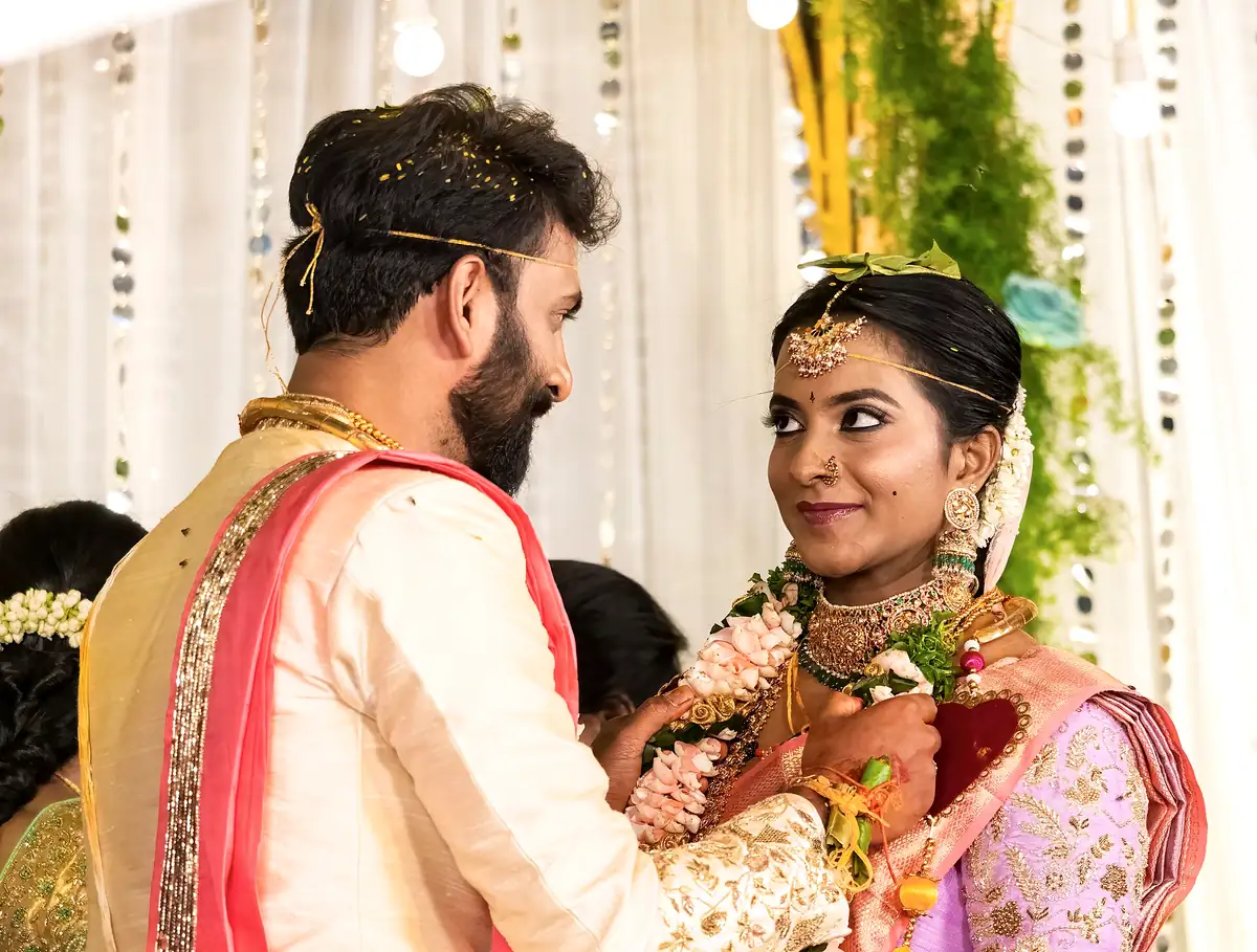 A bride smiles up at the groom as garlands are exchanged, jasmine in her hair